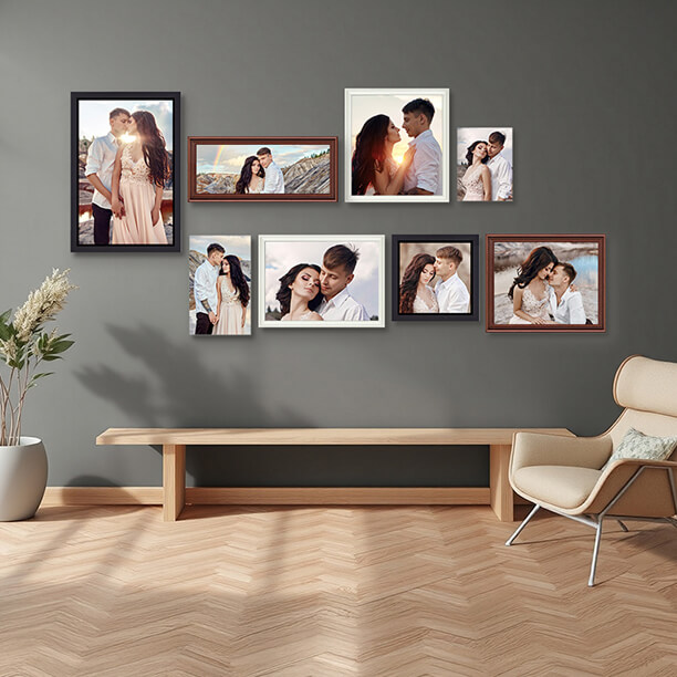 A gallery wall with eight framed couple portraits arranged in a staggered layout above a wooden bench against a dark gray wall.