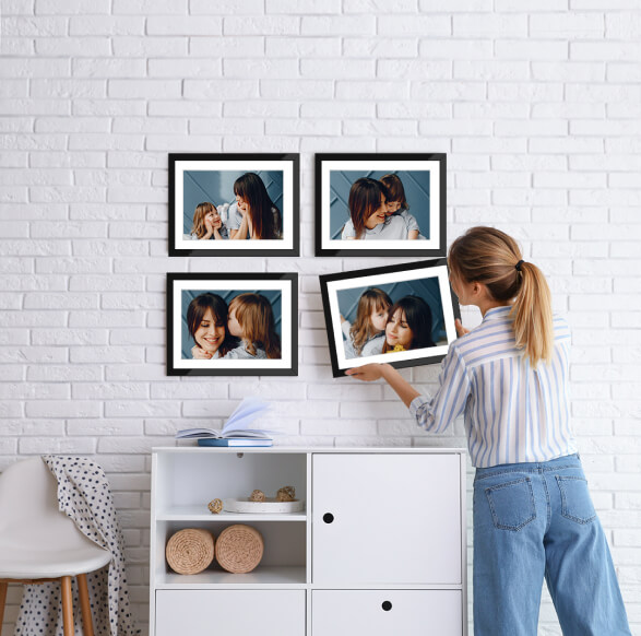 Woman hanging a framed photo on a white brick wall alongside other framed family pictures.